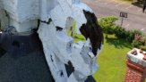 Close up of side bracket with paint peeled away, showing rotted wood, with ground in the distance below.