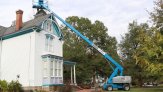 View of the 2-story house with the entire lift visible, with the carpenter working at the peak of the tower, about 45 feet high.