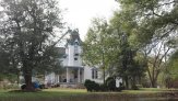 Looking from Montgomery Street at the house, with the lift up to the top of the tower and the carpenter working up there.  There are trees and bushes in the front yard.