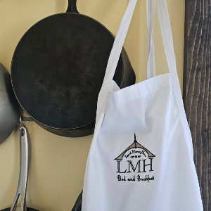 white apron with LMH logo hangs on a hook with skillets