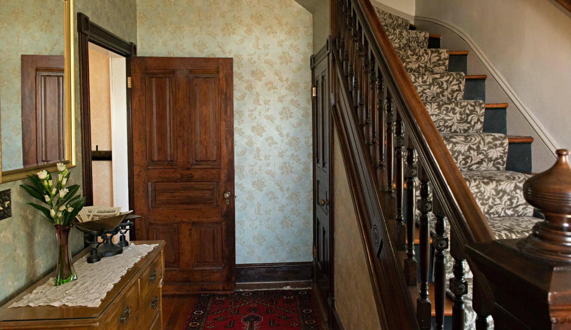 Cream wallpapered hallway with brown wooden staircase to the right and a wooden decorative table against the left wall