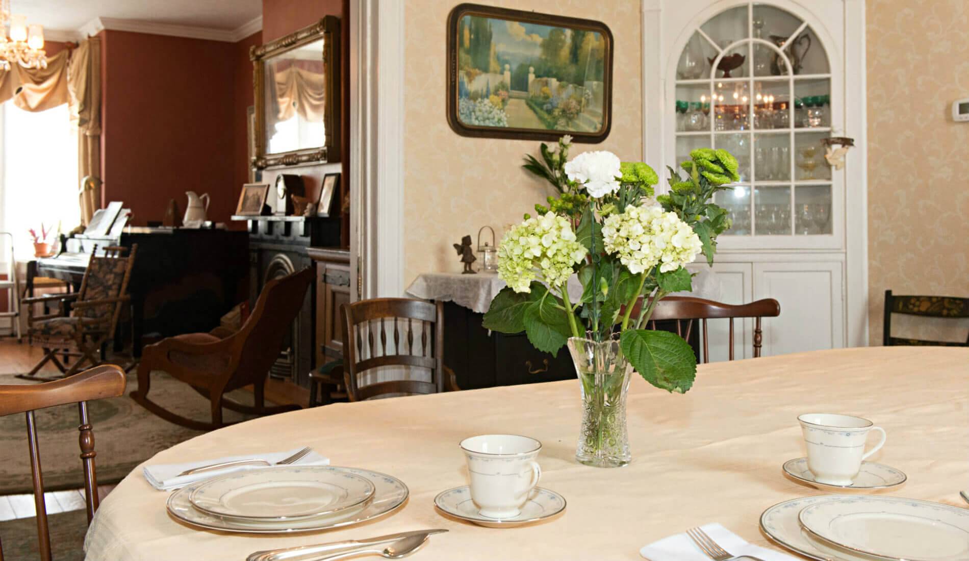 Cream wallpaper dining room, an oval table with a white tablecloth, a glass vase of white flowers