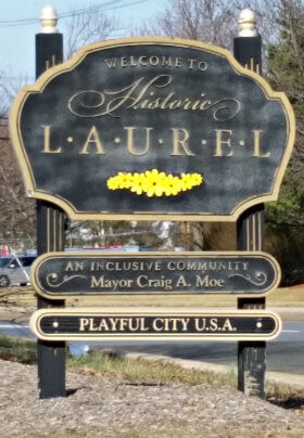 Large exterior black and beige sign that says welcome to historic laurel, an inclusive community, playful city USA