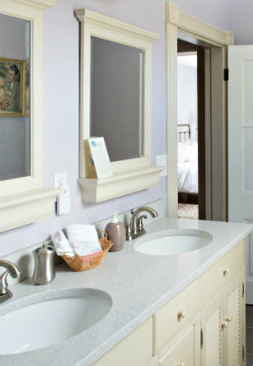 Light purple bathroom with duel rounded sinks, a cream vanity and two cream framed mirrors