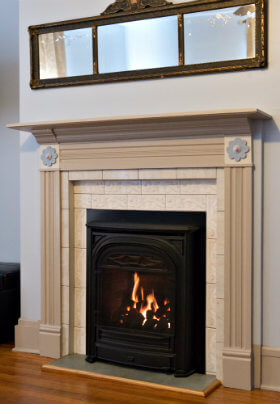 Small black fireplace framed with a beige mantel beneath a mirror