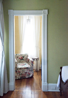 White framed doorway into a yellow room with a floral chair and small metal side table